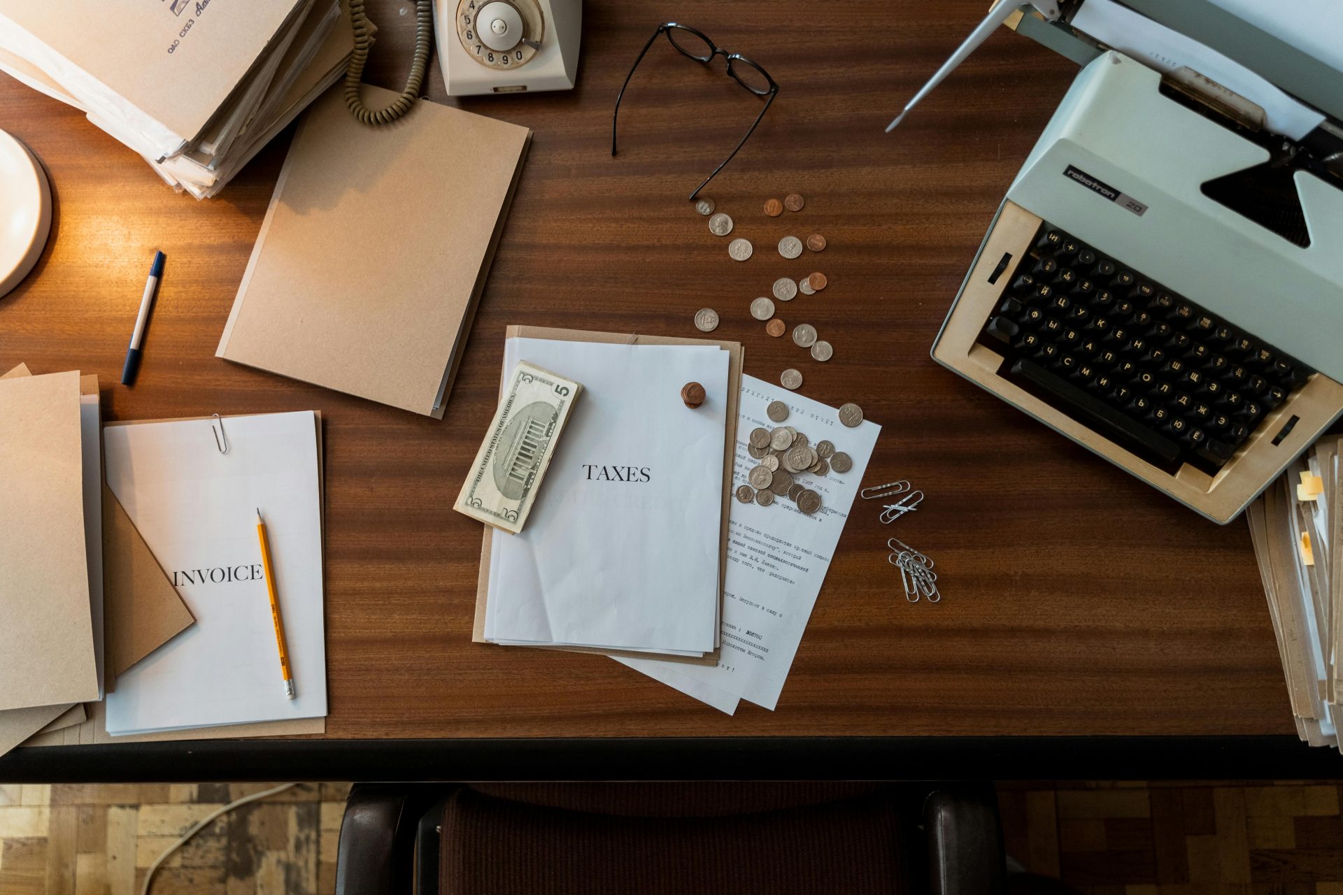 Retro office scene featuring a typewriter, coins, documents, and stationary on a wooden desk.